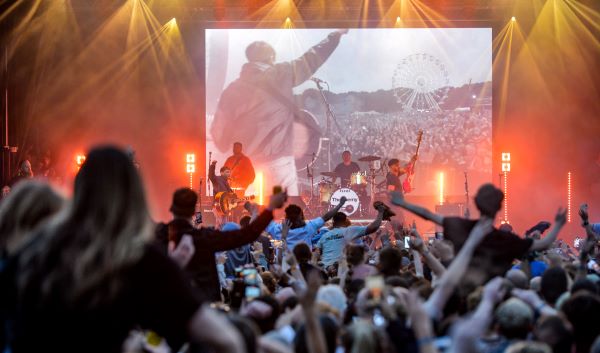 View from behind the crowd looking onto the stage, hands in the air and view of the band performing on stage