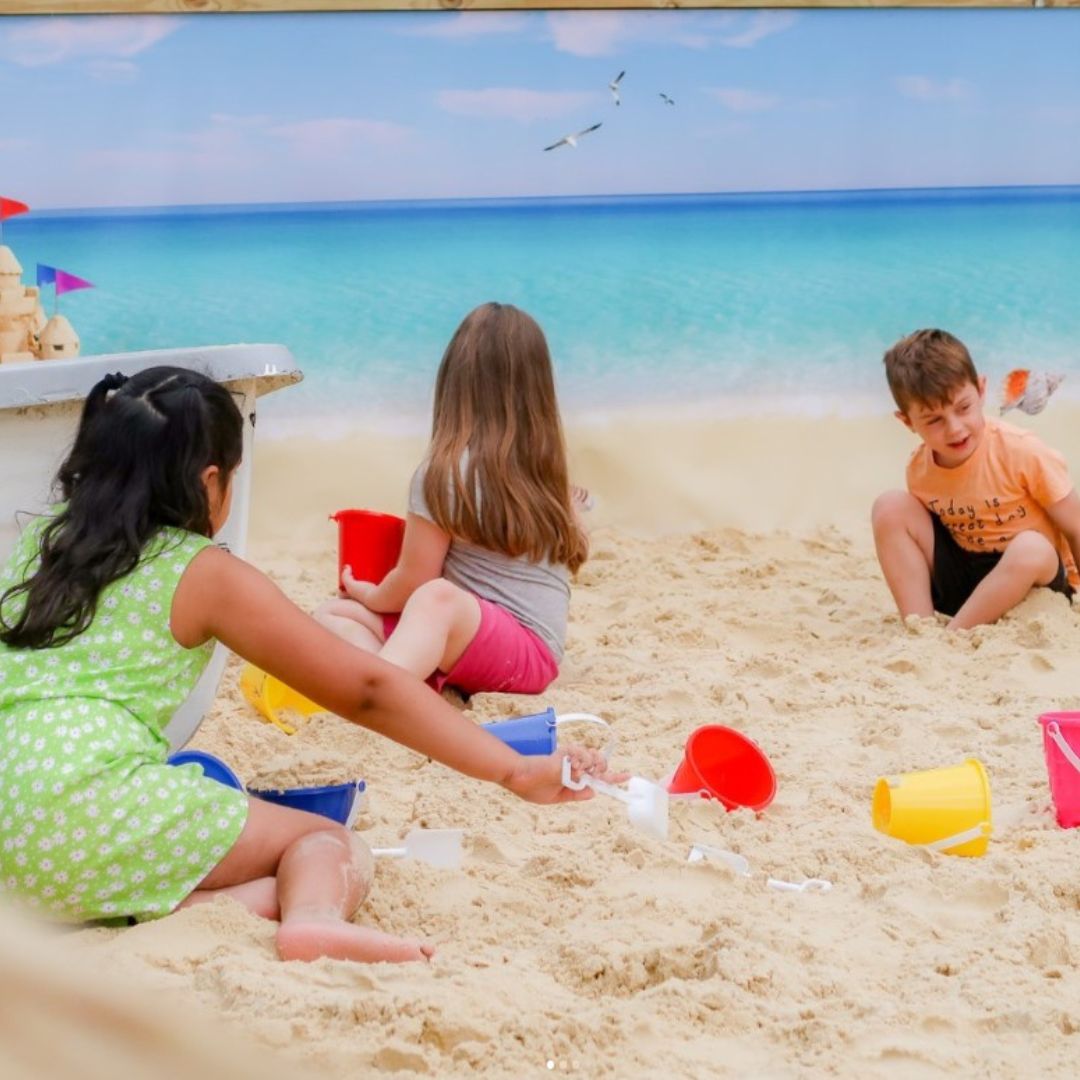 Three children sat in the sand at a pop up beach